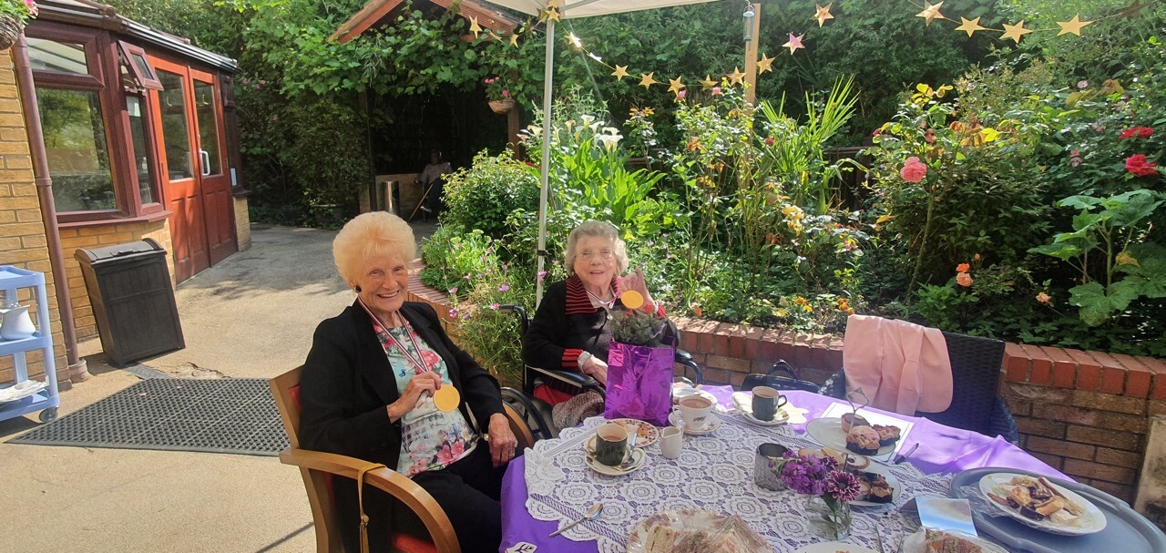 Two ladies sitting in a garden having afternoon tea