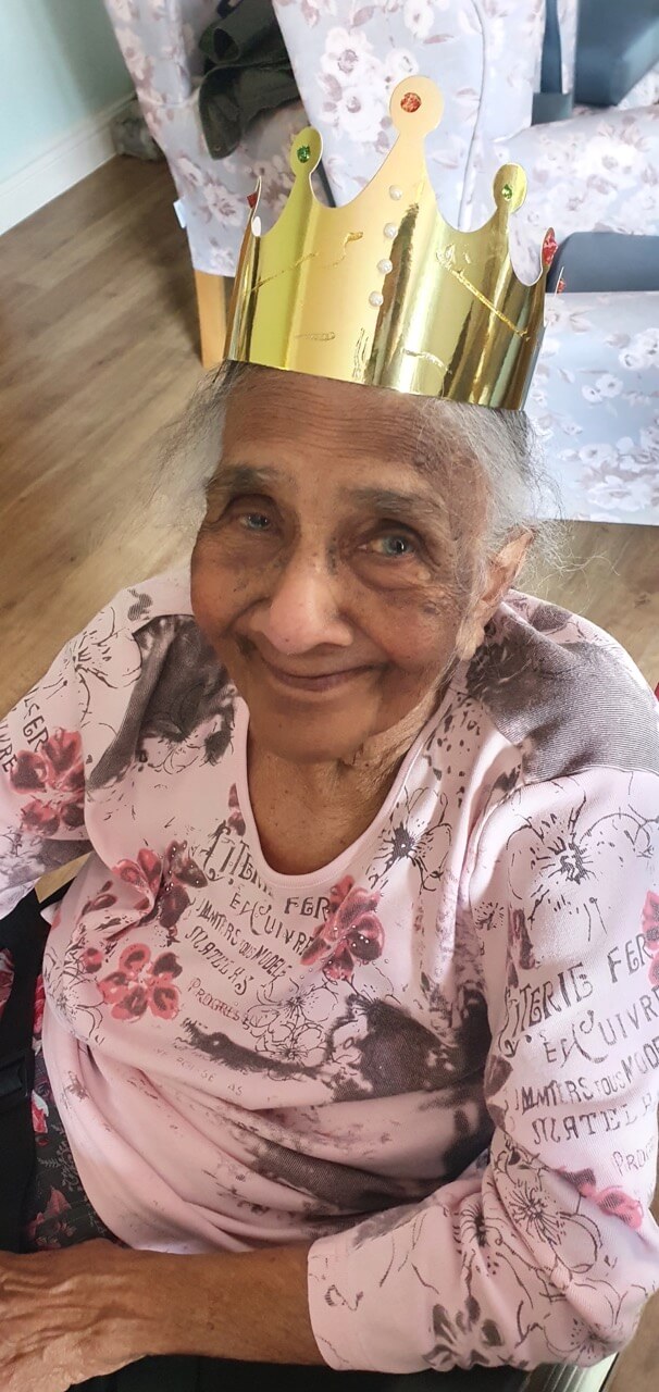 An elderly lady sitting with a gold party hat on her head